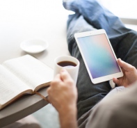 Mann mit iPad und Kaffee in der Hand vor Bibel, die auf dem Tisch liegt.