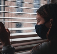 Frau mit Gesichtsmakse schaut aus dem Fenster